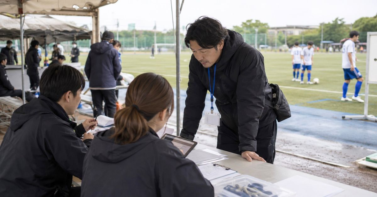 サッカー公式戦の本部席で大会規定や使用機器について確認する監督と運営スタッフ