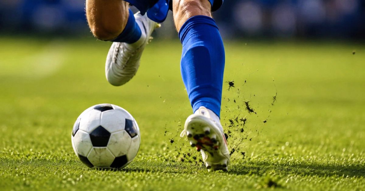 芝生の上でサッカーボールを蹴りながら走る選手の足元