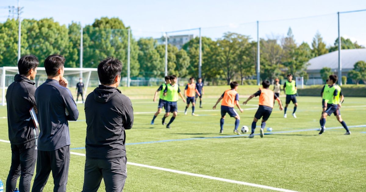 大学サッカーのセレクションでビブスを着た選手のミニゲームを見守るスタッフ
