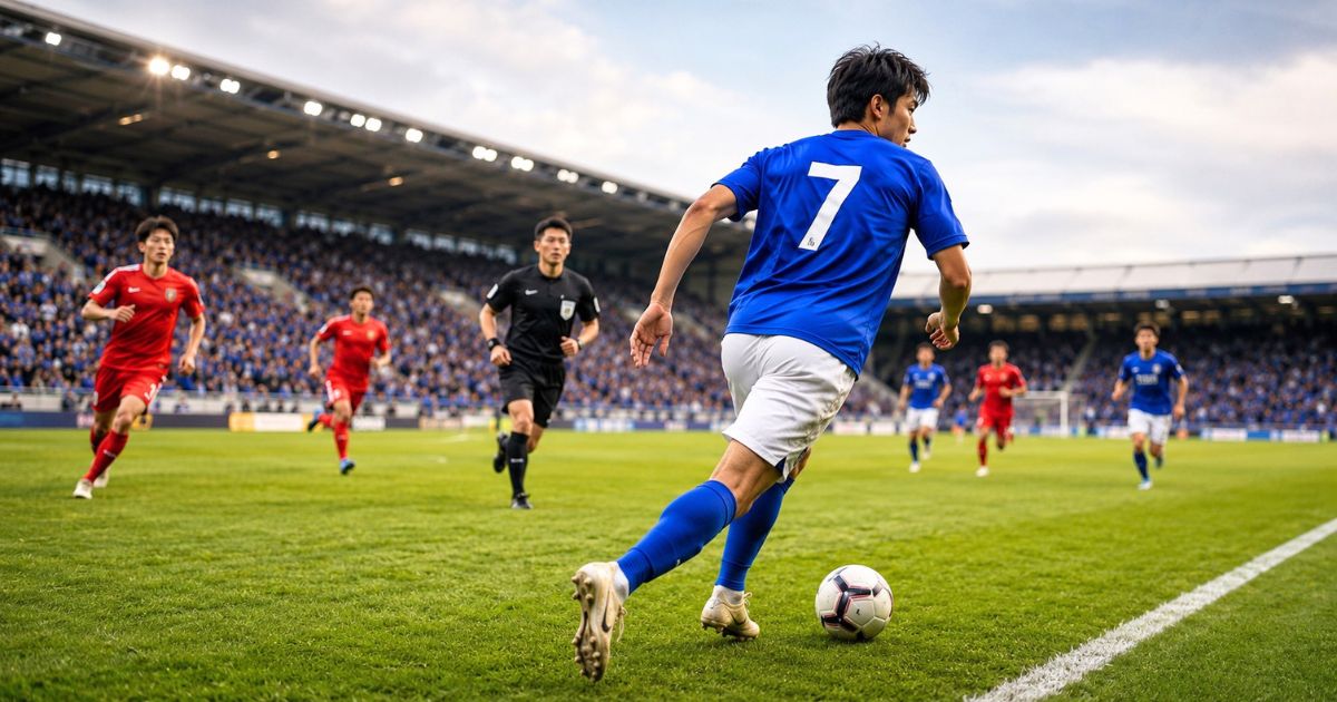 背番号7の青いユニフォームを着た日本人サッカー選手が、審判の見える試合中のピッチでサイドをドリブルする様子
