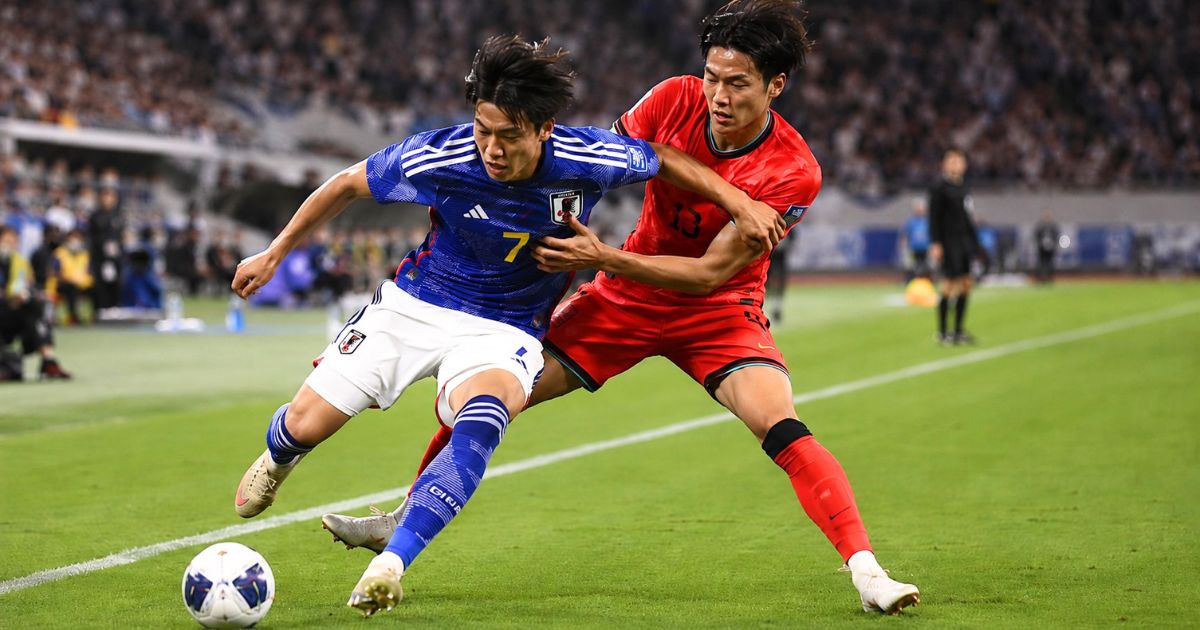 背番号7の青いユニフォームを着た日本人選手が相手選手とボールを競り合うサッカーの試合シーン