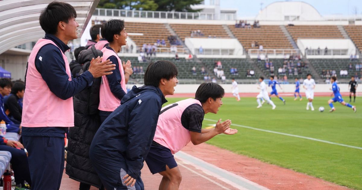 大学サッカーの公式戦で、ベンチから仲間を応援する途中出場候補の選手たち