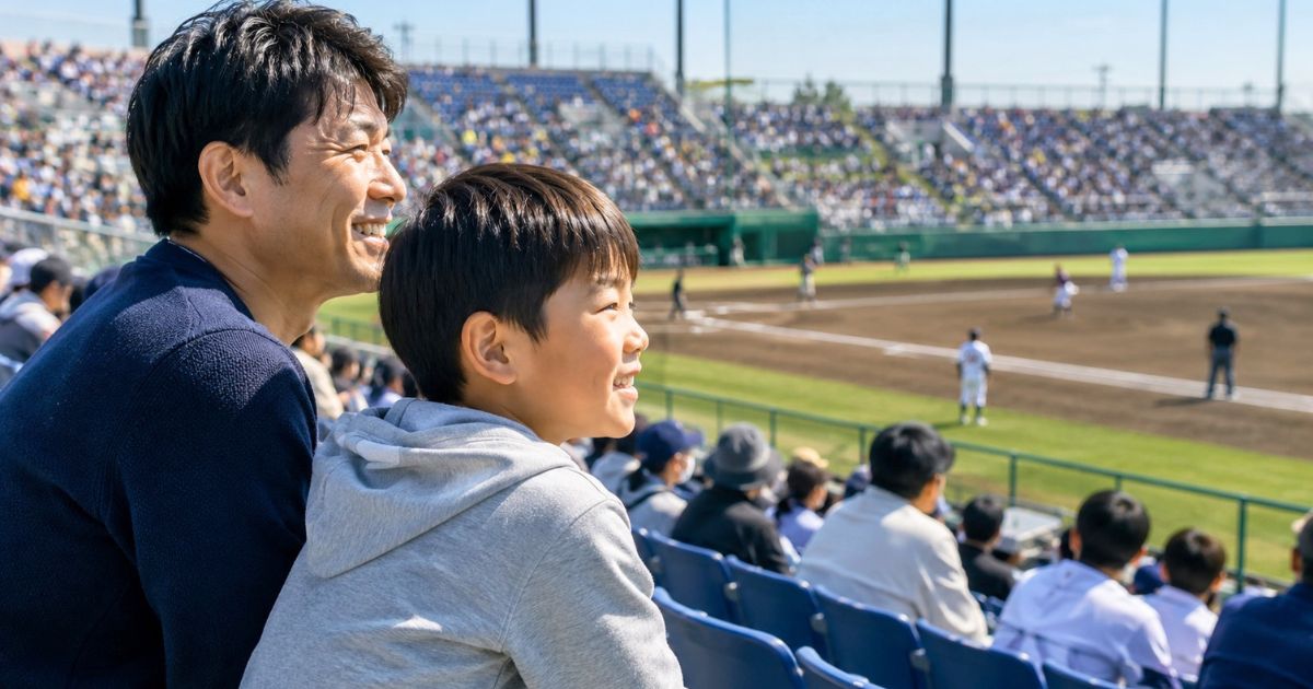 野球場の観客席で、小学生の子どもと父親が笑顔で試合を観戦する様子