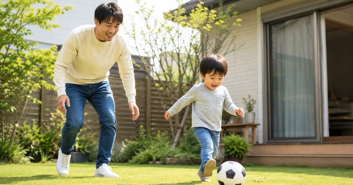 自宅の庭でサッカーボールを追いかけて遊ぶ日本人の父親と3歳くらいの子ども