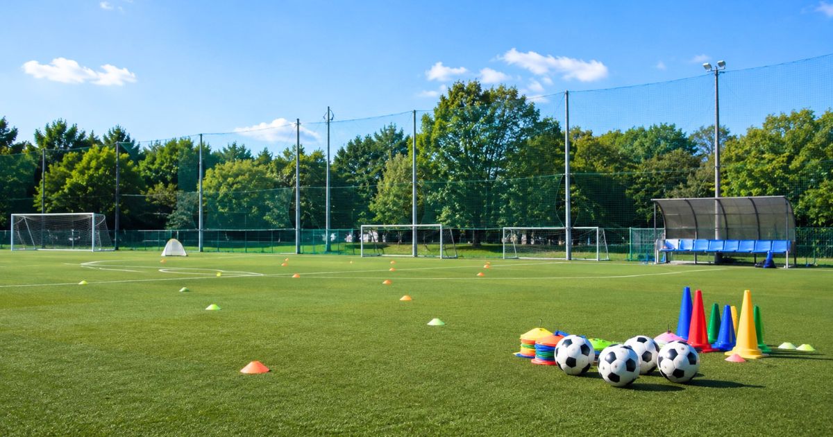 サッカーボールやコーン、ゴールが配置された人工芝の少年サッカー練習場