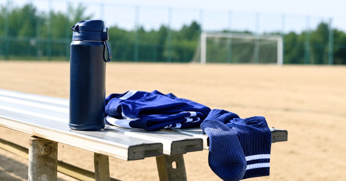 少年サッカーの練習グラウンド脇のベンチに置かれた水筒、青い練習着、サッカーソックス