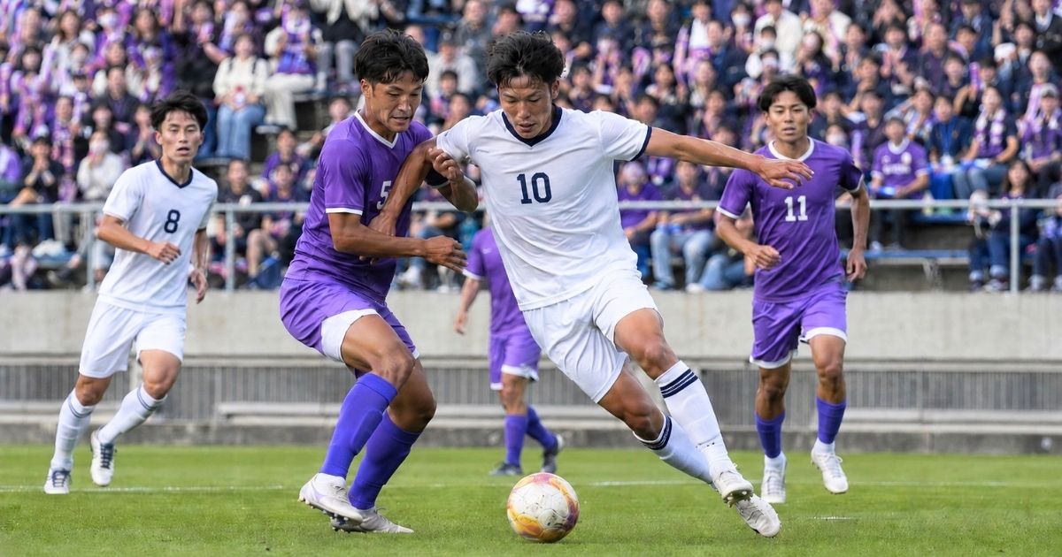 関西学生サッカーリーグの公式戦で、観客席を背に大学選手が激しくボールを競り合う様子
