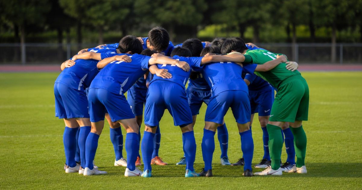 関西学生サッカーリーグの昇格・降格プレーオフを前に、試合直前のピッチで円陣を組む大学サッカー選手たち