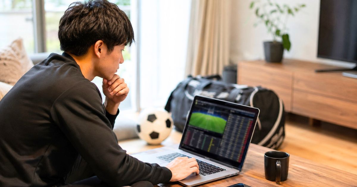 自宅のリビングでサッカー部員がパソコンを使い、関東大学サッカーリーグの順位と試合速報を確認する様子