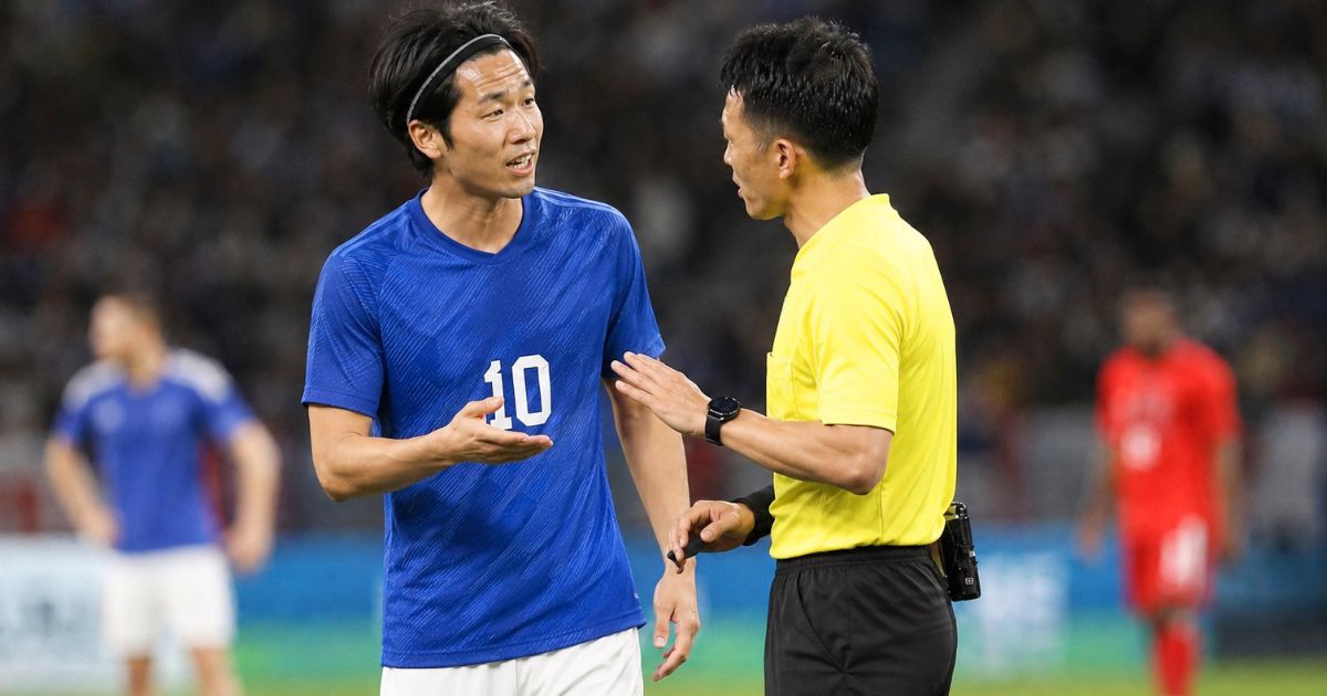 ヘアバンドを着けたサッカー選手が試合中に審判と向かい合って話をしているシーン