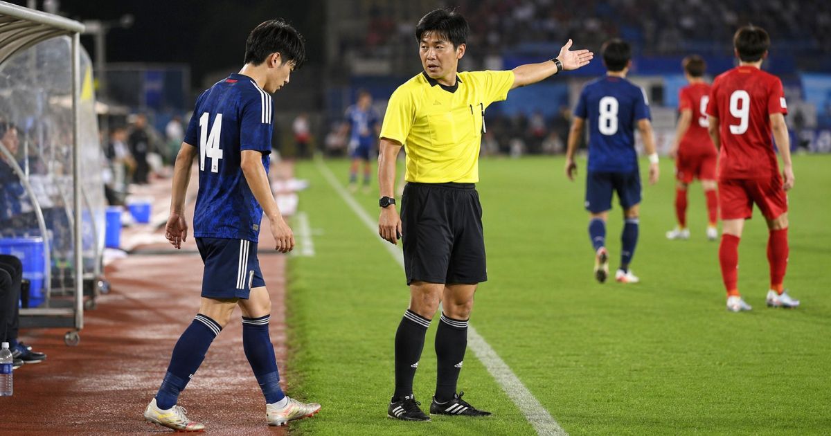 サッカーの試合中、主審の指示を受けた選手が用具を直すため一時的にピッチの外へ出る様子