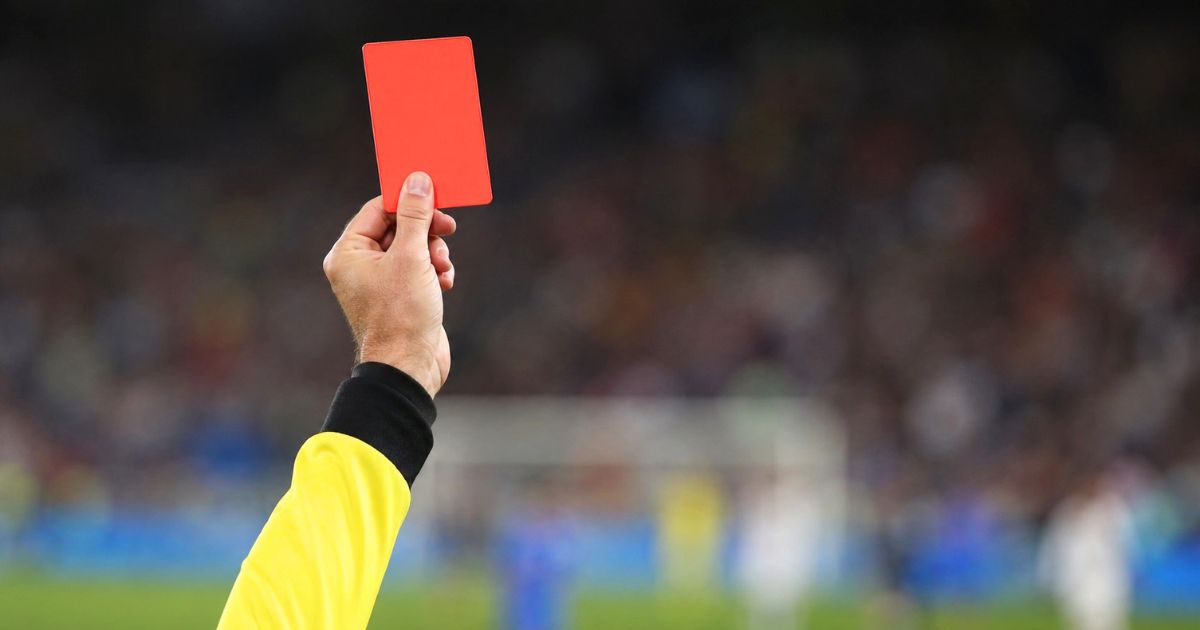 サッカーの試合中、審判が赤いカードを高く掲げている手元のクローズアップ