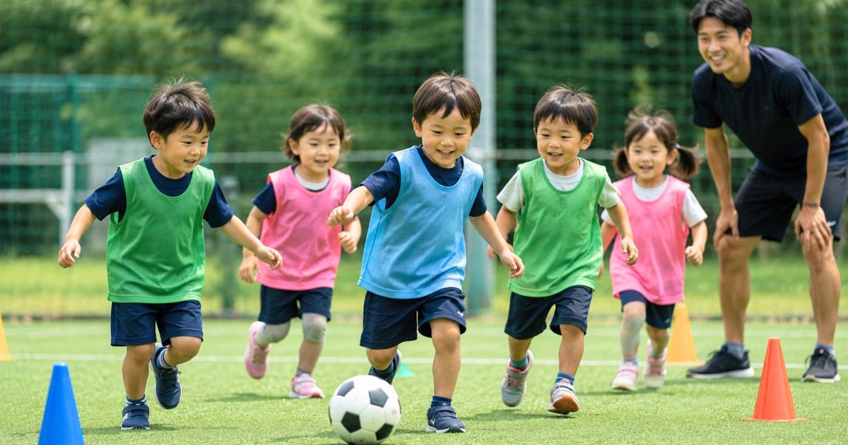 ビブスを着た3歳くらいの子どもたちがボールを追いかけ、若いコーチが見守る幼児向けサッカー練習風景