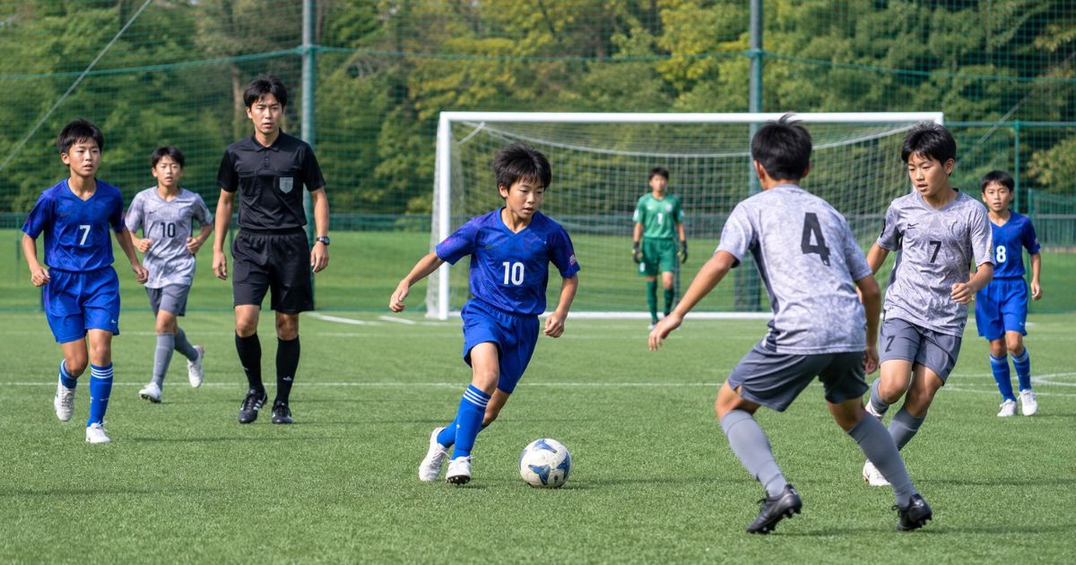 U-12年代の8人制サッカーで、青いユニフォームの選手がドリブルし、相手選手と審判がプレーを見守る試合風景