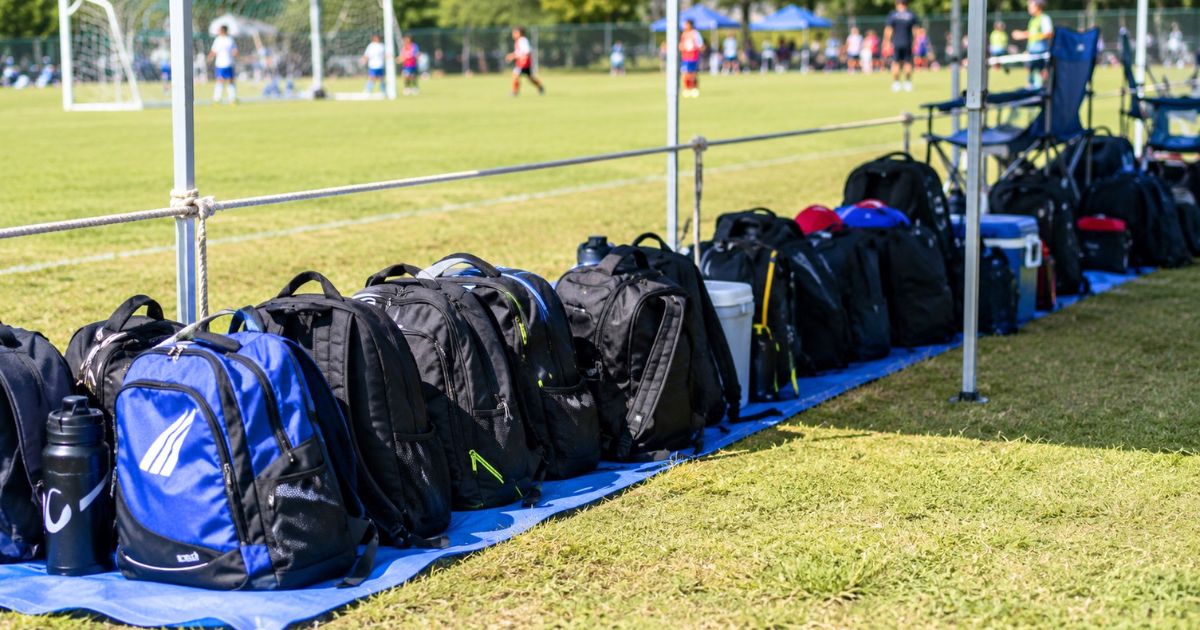 U-12少年サッカーの試合会場で、コート脇の荷物置き場に並べられたリュックや水筒