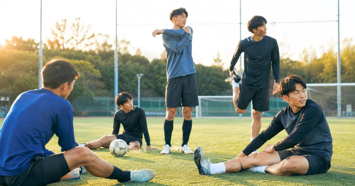 大学のサッカーグラウンドで練習前にストレッチする大学生選手たち