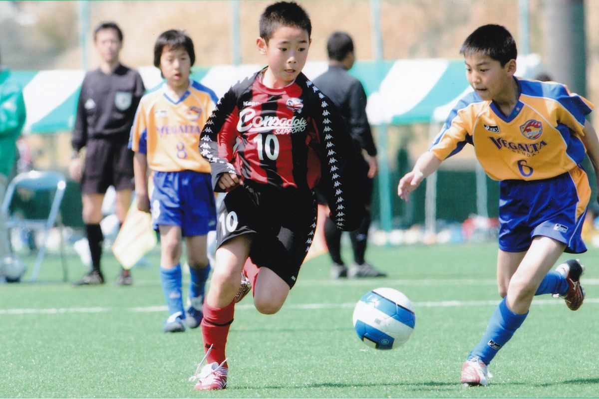 コンサドーレ札幌U-12のユニフォームを着た選手が試合でドリブルする様子