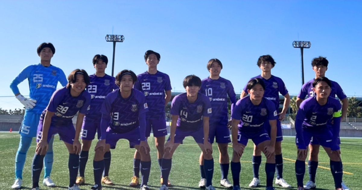 富士大学サッカー部の選手たちが紫のユニフォーム姿でサッカー場に並ぶ集合写真