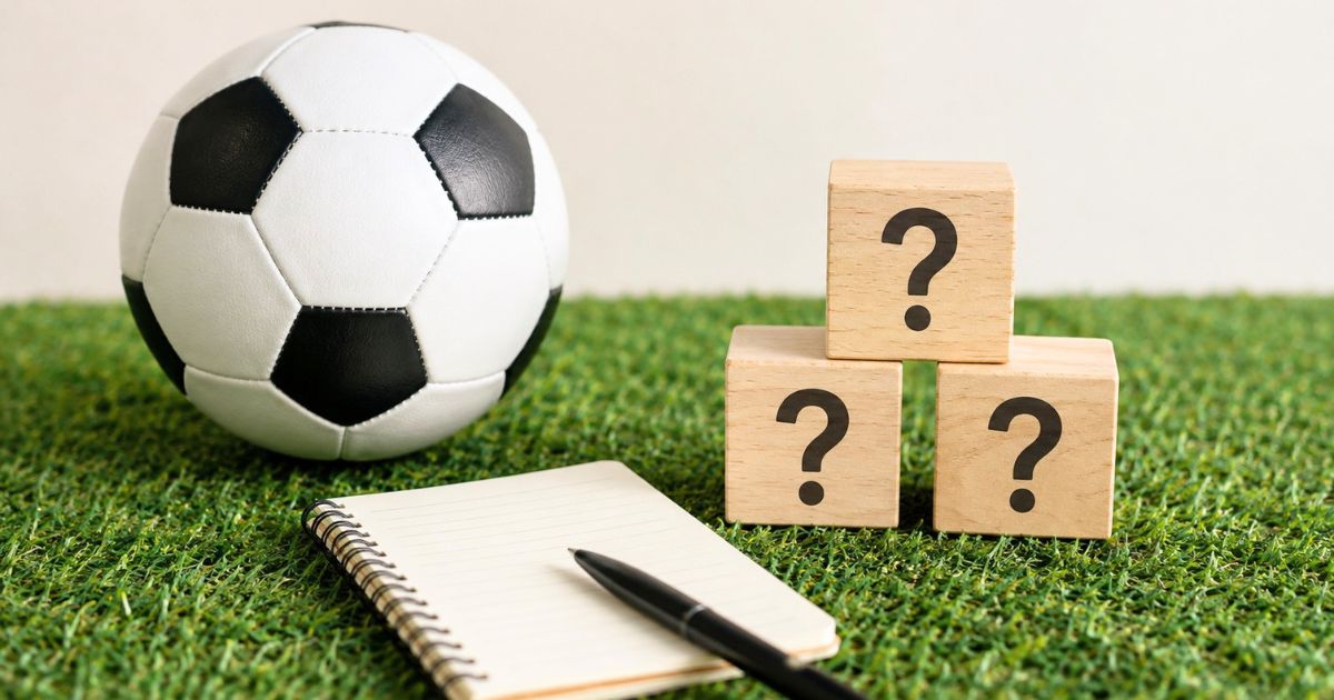 人工芝の上に置かれたサッカーボール、ノート、疑問符の積み木で高校サッカー費用のFAQを表現した画像