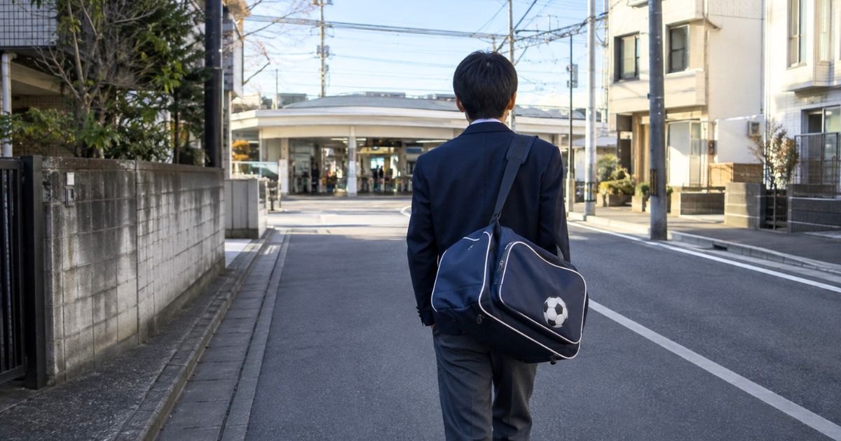 サッカーバッグを肩に掛け、通学のため住宅街から駅へ向かう制服姿の高校生サッカー部員
