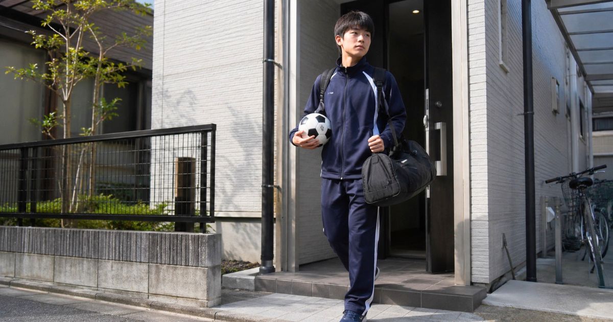 民間寮からサッカーボールと荷物を持って登校する高校サッカー部員
