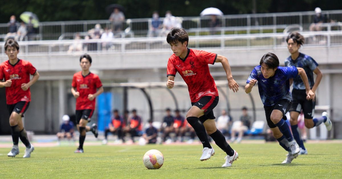 大阪大学サッカー部のリーグ公式戦をイメージした赤いユニフォームの選手が競り合う試合風景