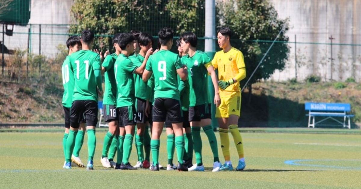 専修大学サッカー部の選手たちが試合前にピッチ上で円陣を組む様子