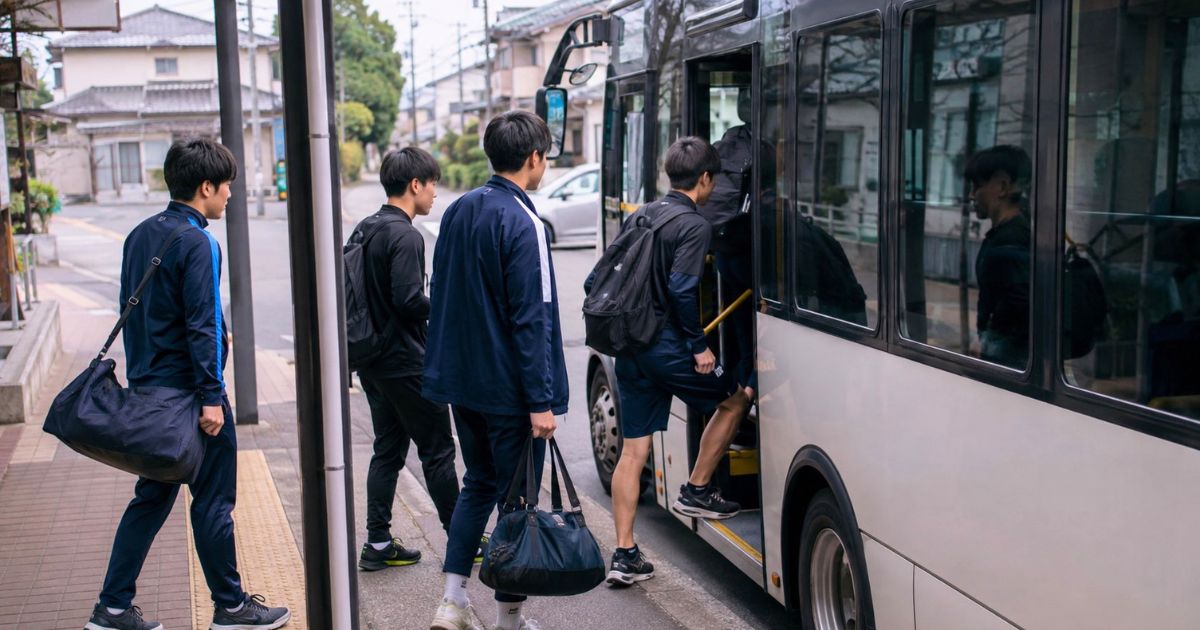 最寄駅付近のバス停から、バッグを持って寮へ向かう大学サッカー部員たちのイメージ