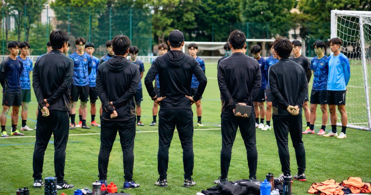 大学サッカー部の練習前にグラウンドで選手へ指示を伝える監督・コーチ陣