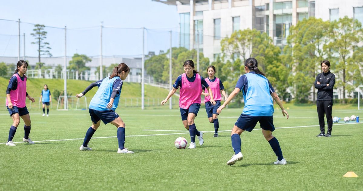 大学女子サッカー部の専用グラウンドで、コーチが見守る中ビブスを着てミニゲームをする女子大学生選手たち