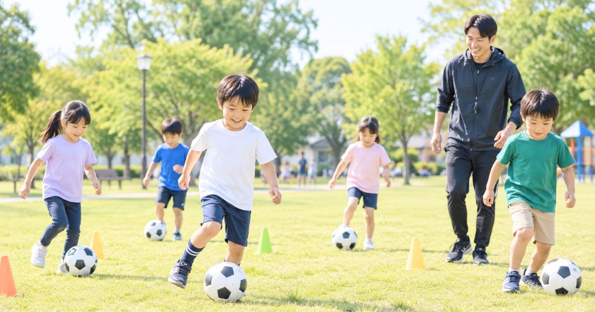 公園の芝生で、コーチと小学生の子どもたちがボールとコーンを使って練習するサッカースクールの様子