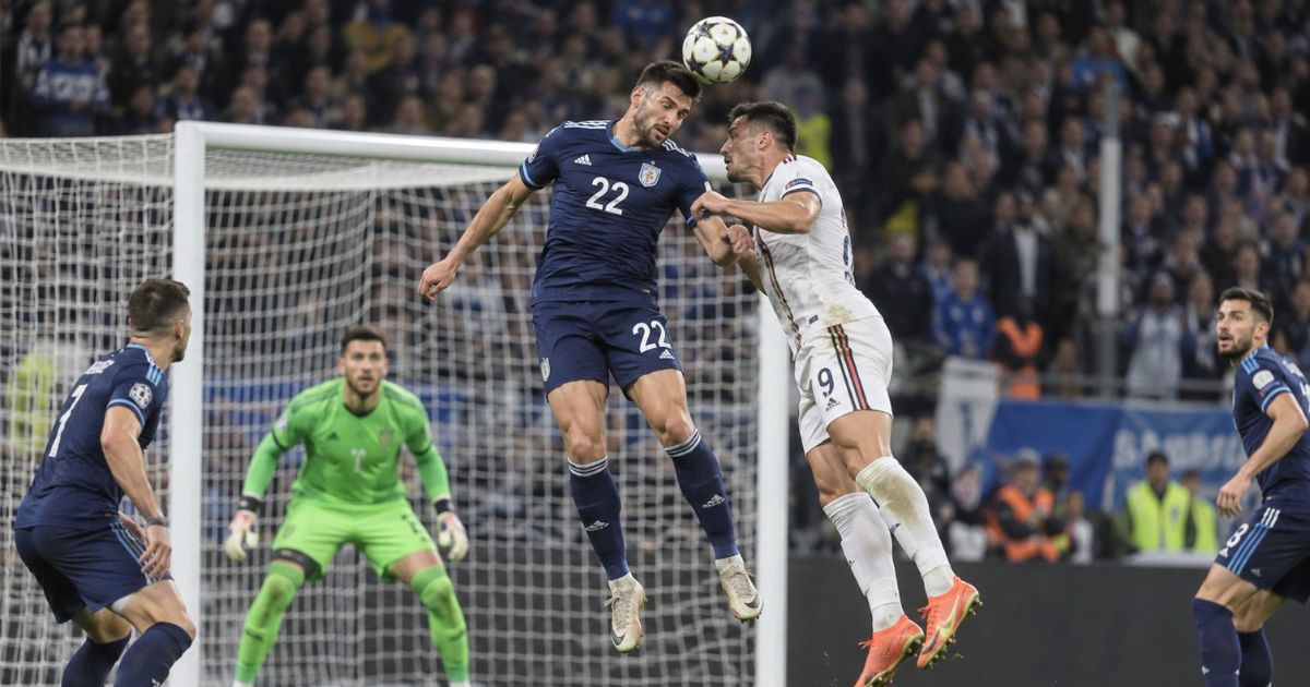 自陣ゴール前で背番号22のサッカー選手が相手選手と空中戦で競り合う場面