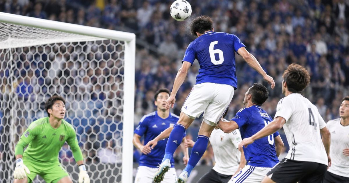 自陣ゴール前で背番号6のサッカー選手が競り合いながらヘディングでクリアする場面