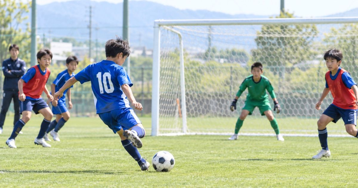 トレセンのミニゲームで、フォワードの少年選手がゴール前からシュートを放ち、ゴールキーパーが構える様子