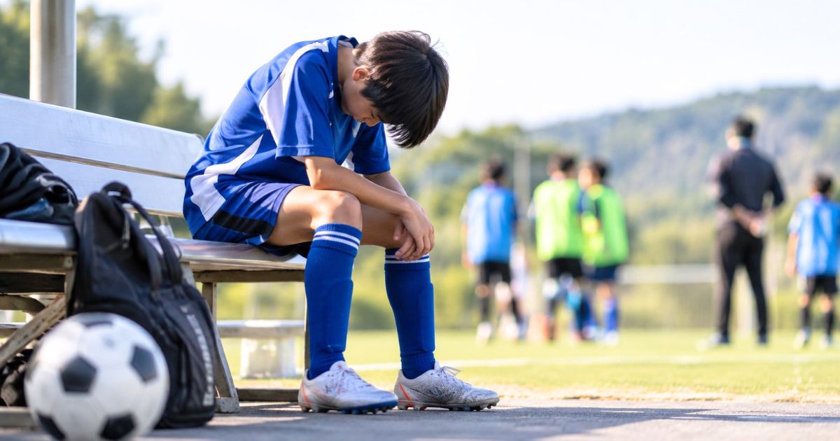 トレセンの選考後、サッカーグラウンド脇のベンチで肩を落として座る少年選手の様子