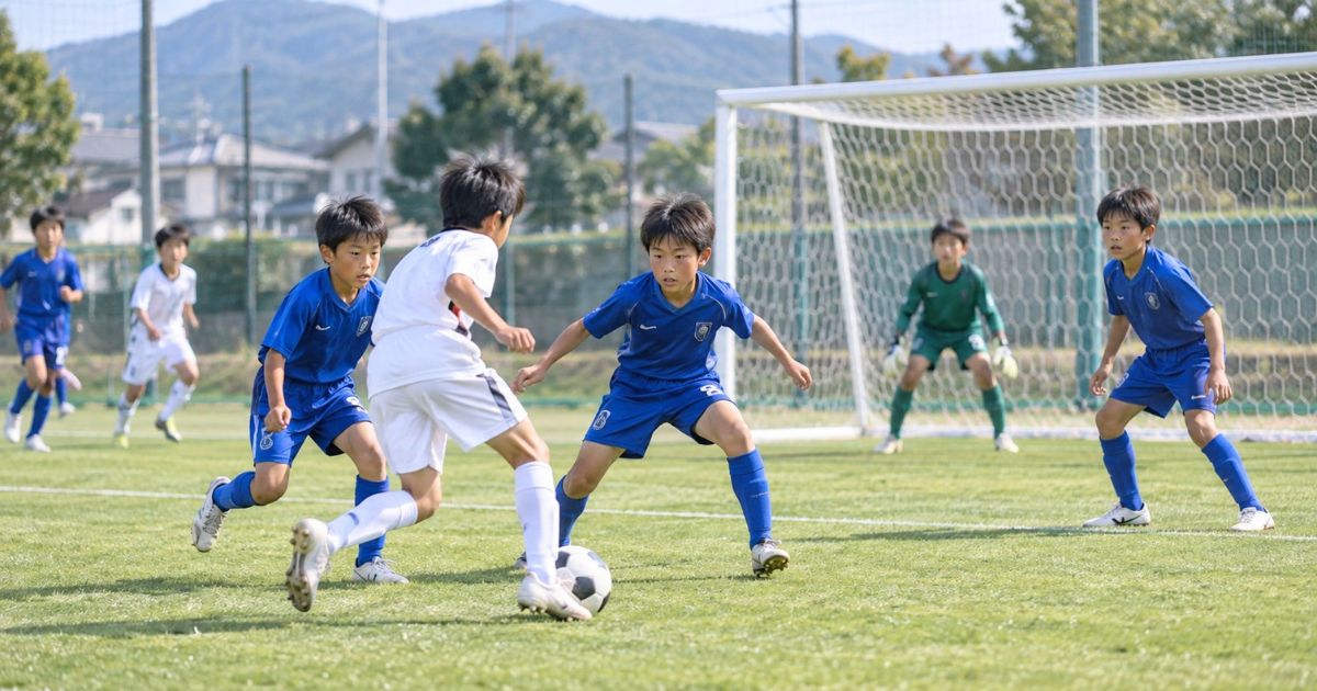 U12年代の8人制サッカーの試合で、ゴール前で青いユニフォームのディフェンス選手たちが相手の攻撃を必死に守るシーン
