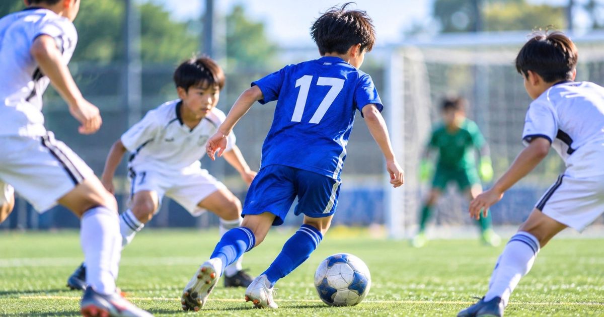 少年サッカーの試合で背番号17の青いユニフォームを着た選手が、相手選手に囲まれながらドリブルする様子