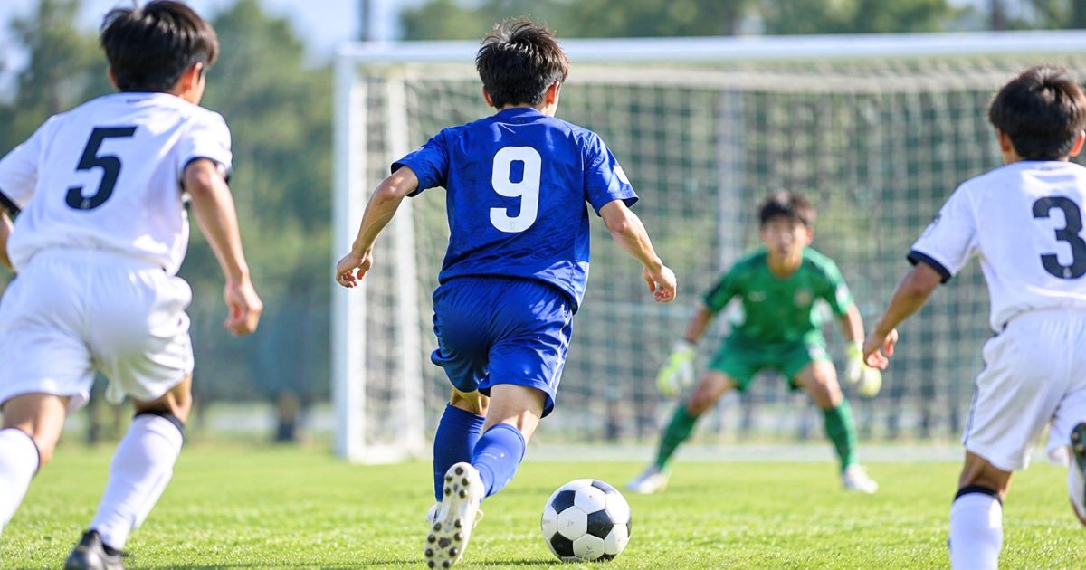 少年サッカーで背番号9の選手が相手ゴールへドリブルする場面