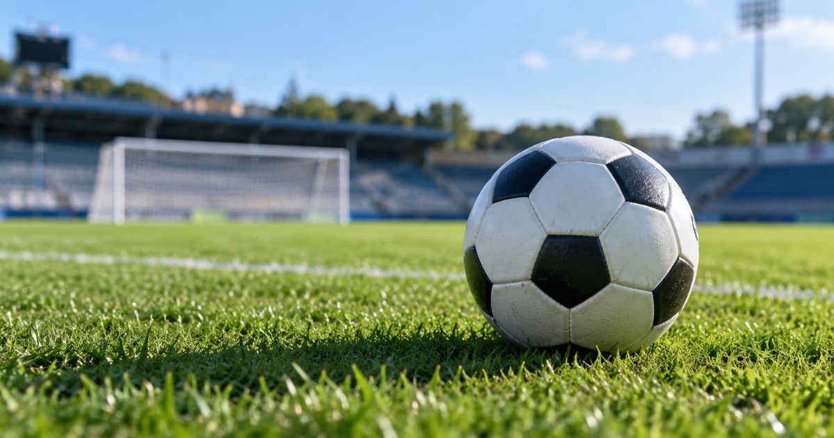 高校サッカーのプレミアリーグ2026をイメージした画像。緑の芝生の上に置かれた白黒のサッカーボールをアップで撮影し、背景にはゴールや観客席が広がっている。