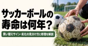 サッカーボールの寿命や買い替えサインを解説するアイキャッチ画像。芝生のグラウンドで、表面にひび割れや傷がある古いサッカーボールを両手で確認している様子。背景には新しいサッカーボールが置かれている。