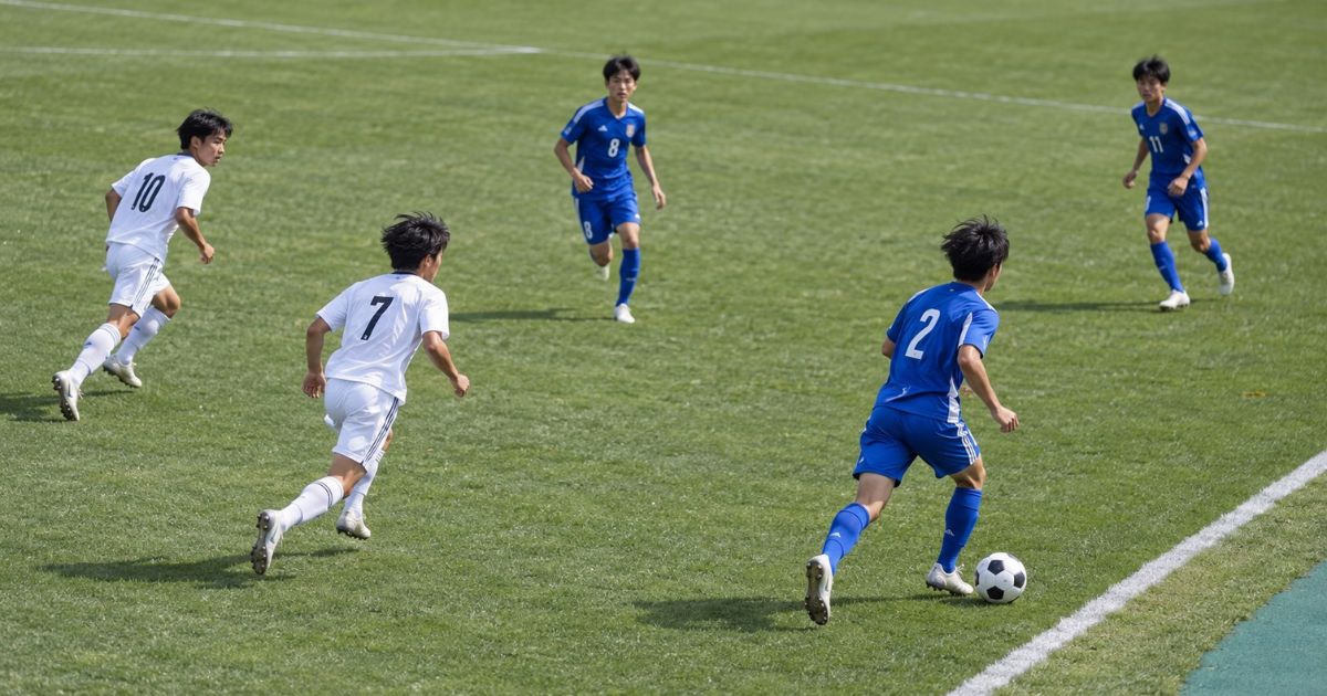 サッカーの試合で、青いユニフォームの右サイドバック(2番)がタッチライン際をドリブルで前進し、味方と連携しながら攻撃参加する様子。